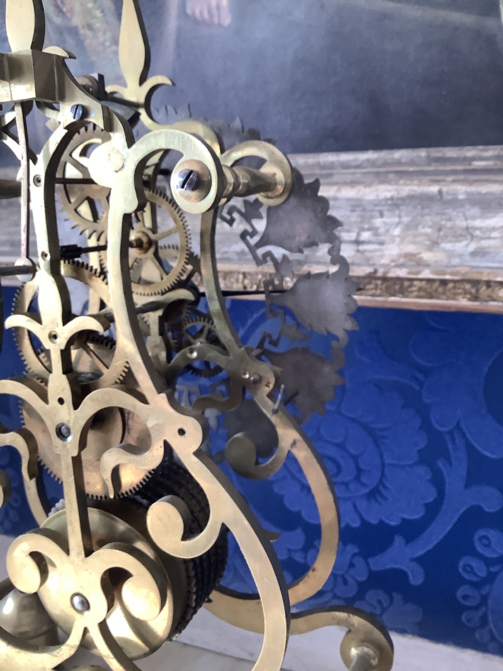 A Victorian brass skeleton clock featuring an openwork frame, pierced chapter ring with Roman numerals, and a white marble plinth base. View XII