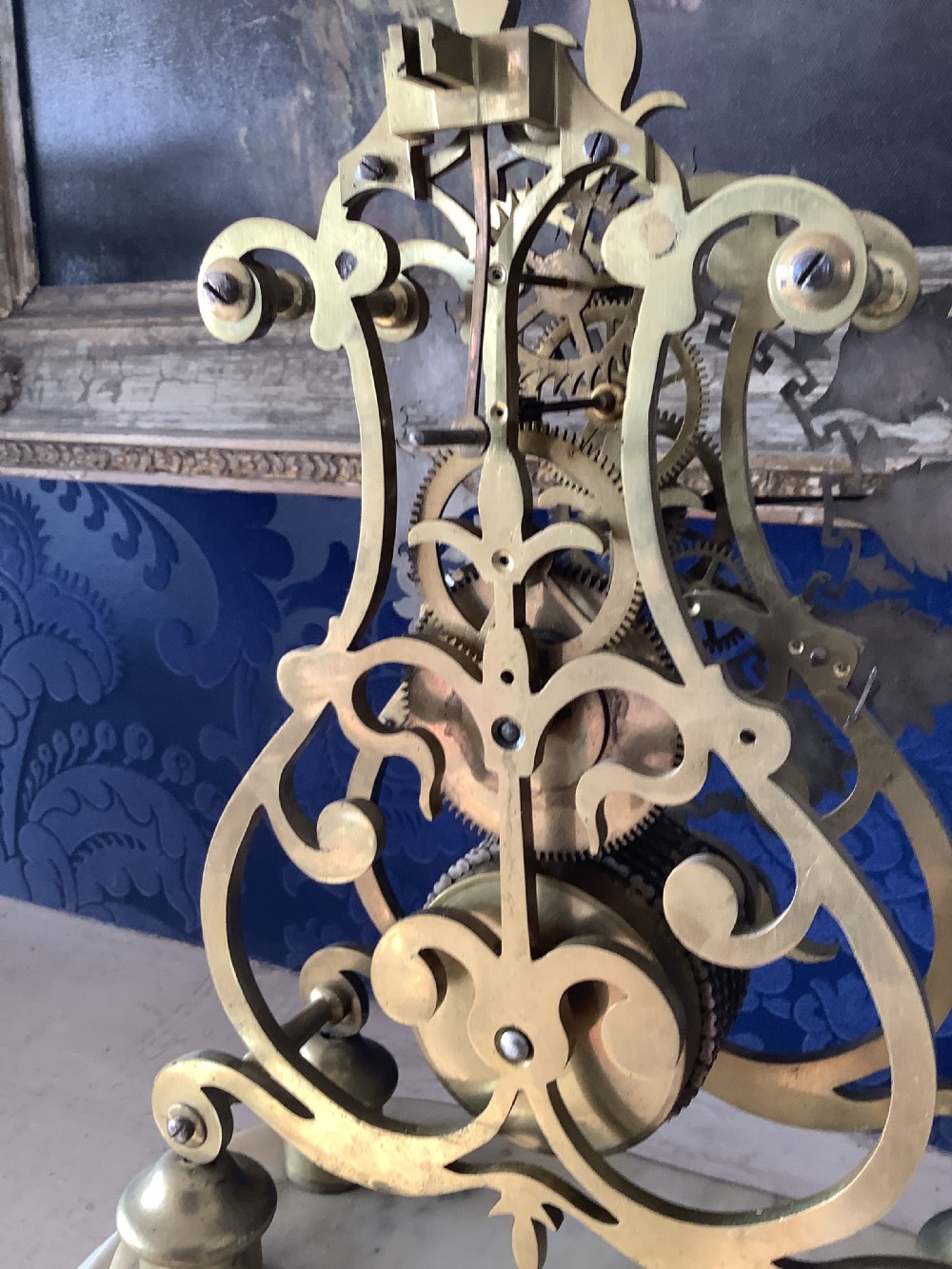 A Victorian brass skeleton clock featuring an openwork frame, pierced chapter ring with Roman numerals, and a white marble plinth base. View XIII
