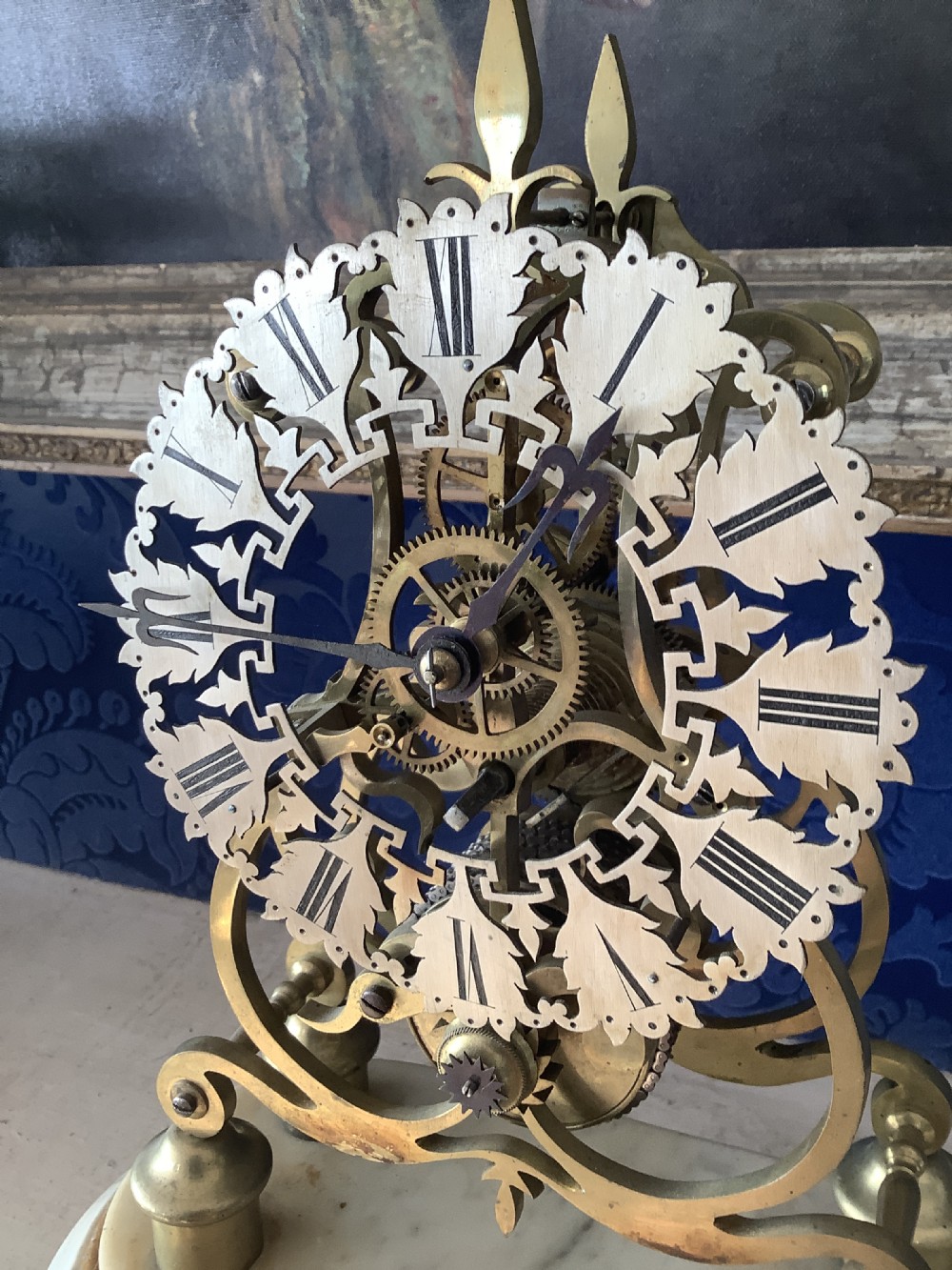 A Victorian brass skeleton clock featuring an openwork frame, pierced chapter ring with Roman numerals, and a white marble plinth base. View XIV