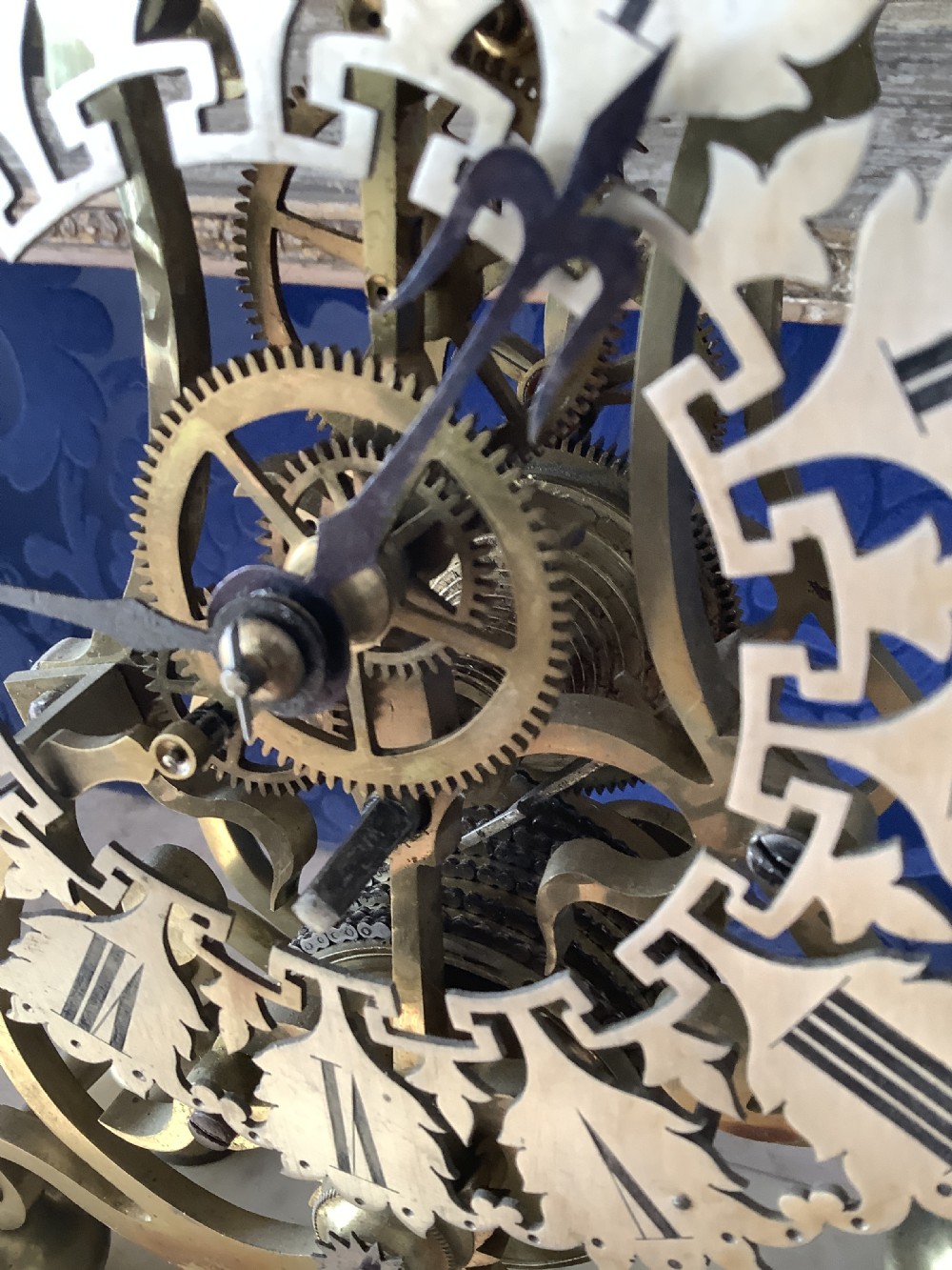 A Victorian brass skeleton clock featuring an openwork frame, pierced chapter ring with Roman numerals, and a white marble plinth base. View XV