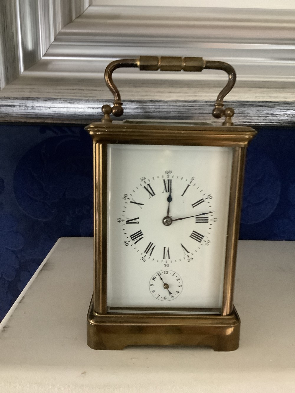 An antique French brass carriage clock featuring a white enamel dial with Roman numerals, a subsidiary dial, and an overhead carrying handle.