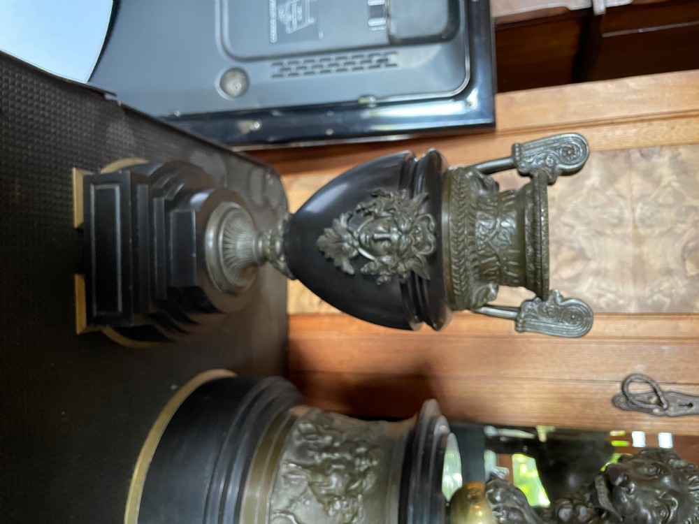 An antique French mantel clock garniture set featuring a black stone clock topped with a bronze lion alongside two matching classical urns. View II
