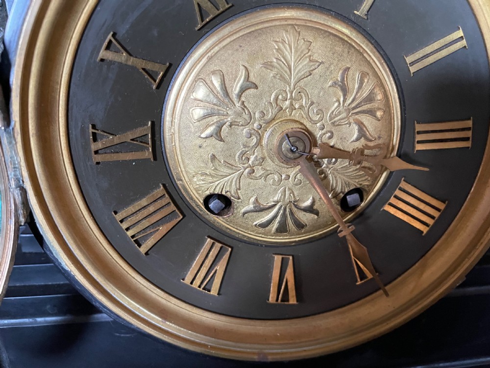 An antique French mantel clock garniture set featuring a black stone clock topped with a bronze lion alongside two matching classical urns. View V