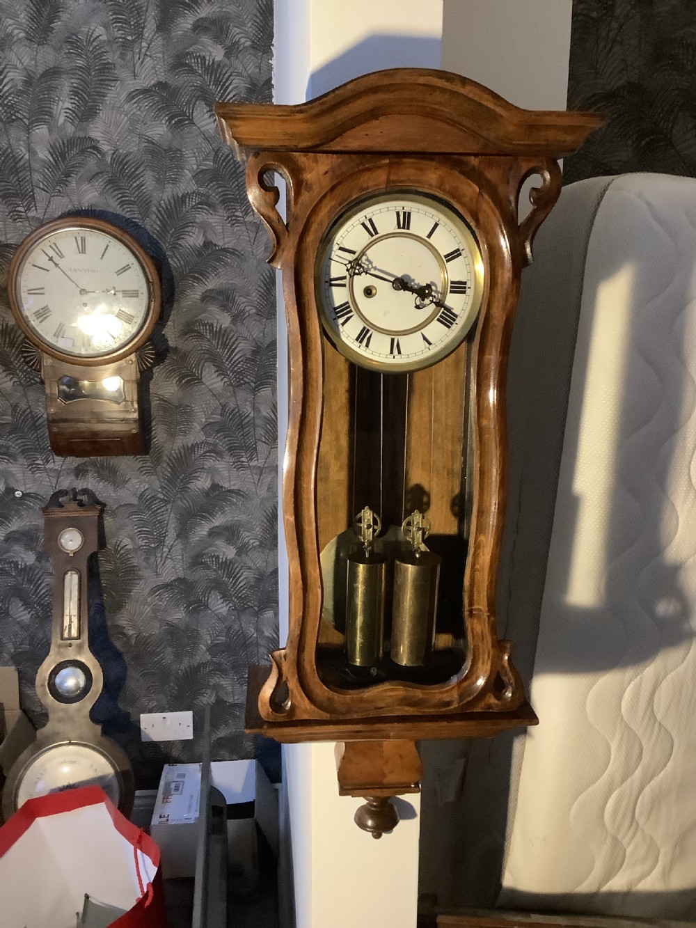 An antique miniature Vienna regulator wall clock crafted from glazed walnut with two brass weights and an enamel dial.