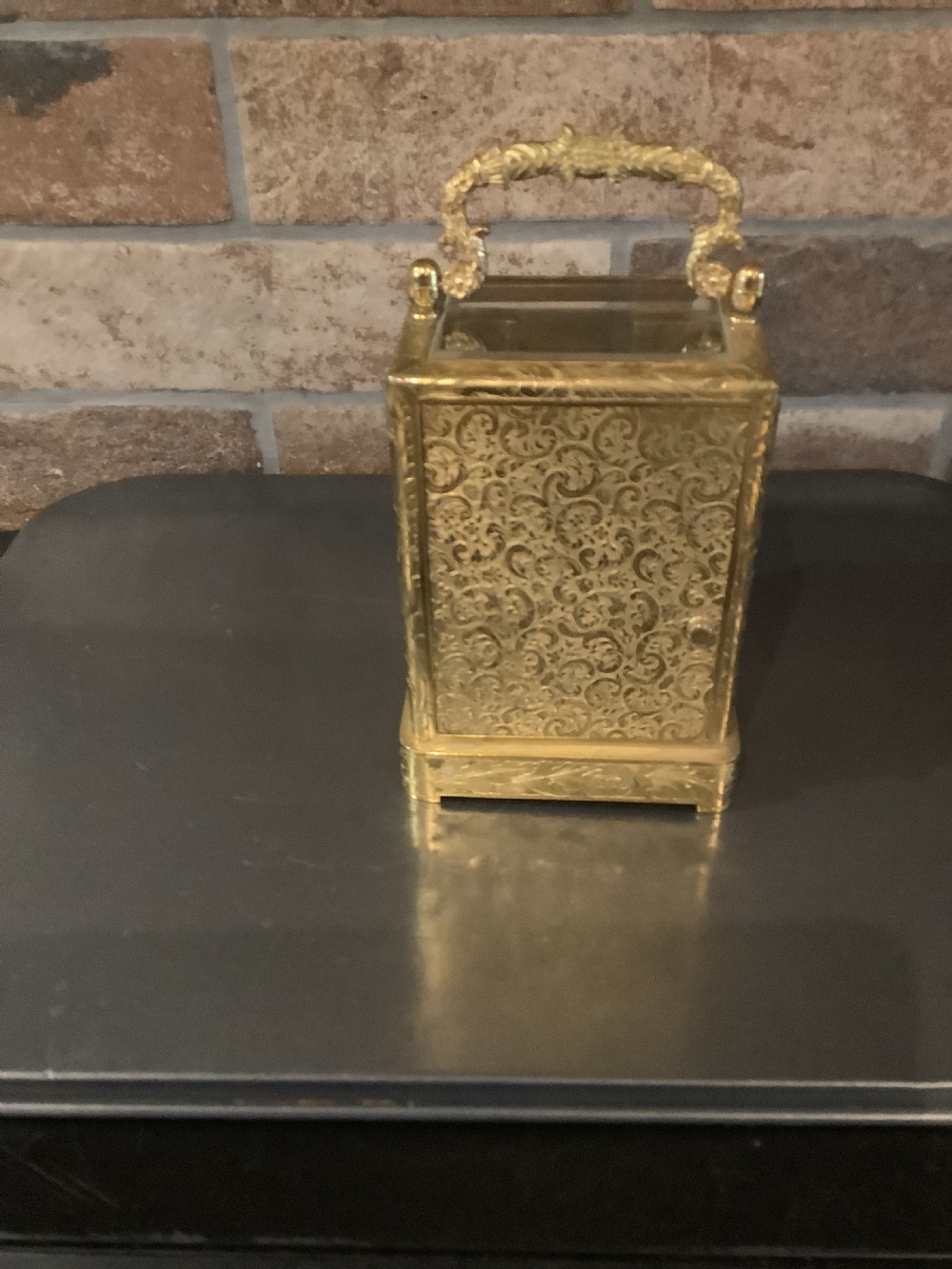 A rectangular gilt brass French carriage clock featuring ornate floral scroll engravings, glass side panels, a decorative carrying handle, and a white enamel dial. View V