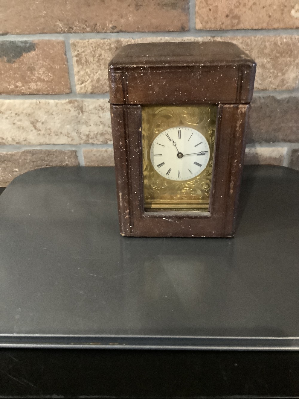 A rectangular gilt brass French carriage clock featuring ornate floral scroll engravings, glass side panels, a decorative carrying handle, and a white enamel dial. View VII