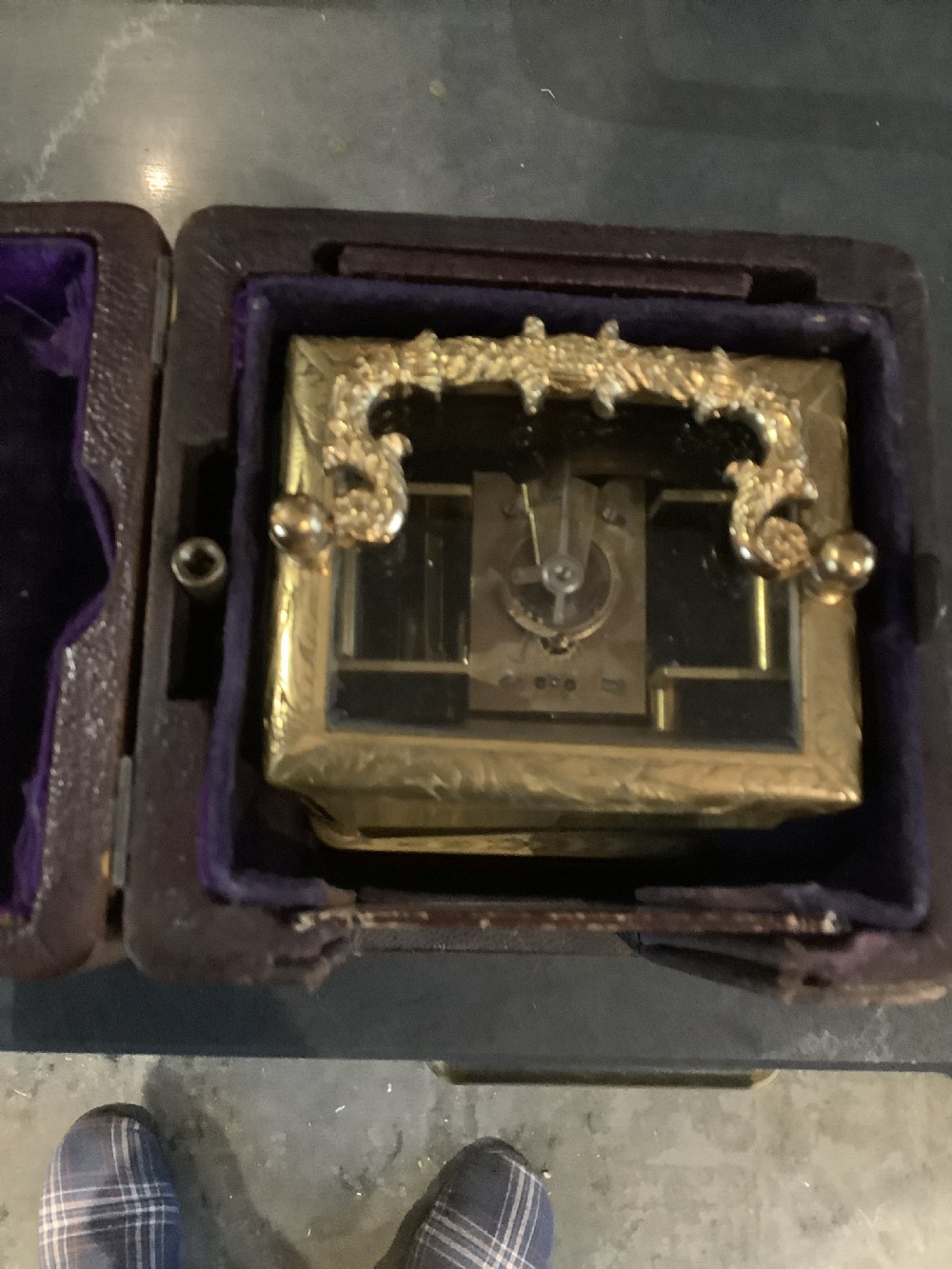 A rectangular gilt brass French carriage clock featuring ornate floral scroll engravings, glass side panels, a decorative carrying handle, and a white enamel dial. View VIII