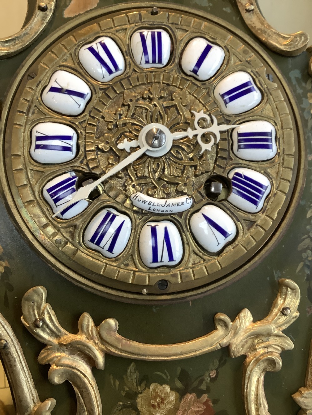 An olive green French Rococo style mantel clock adorned with painted flowers, gilded bronze scrollwork mounts, and an enamel cartouche dial. View VIII
