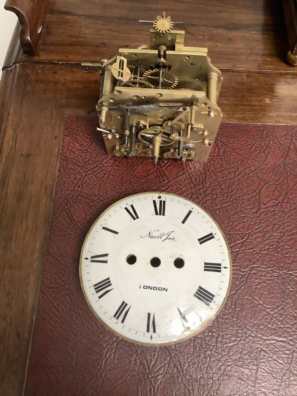 A Regency period wooden table clock with brass inlay, a pediment top, brass lion-head side handles, and a white dial displaying Roman numerals. View IV