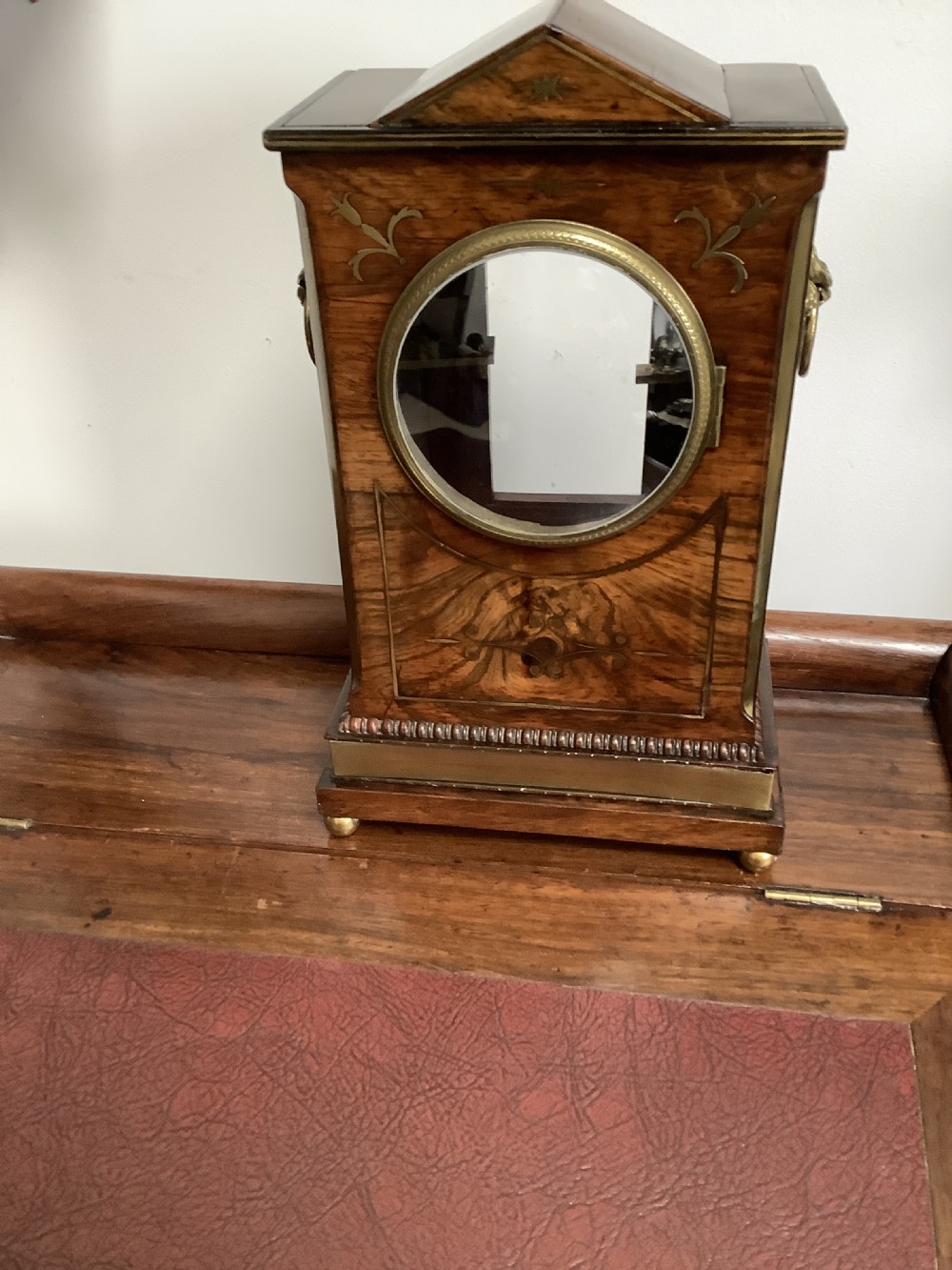 A Regency period wooden table clock with brass inlay, a pediment top, brass lion-head side handles, and a white dial displaying Roman numerals. View VIII