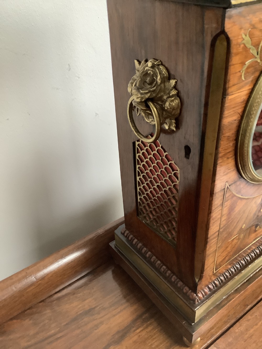 A Regency period wooden table clock with brass inlay, a pediment top, brass lion-head side handles, and a white dial displaying Roman numerals. View IX