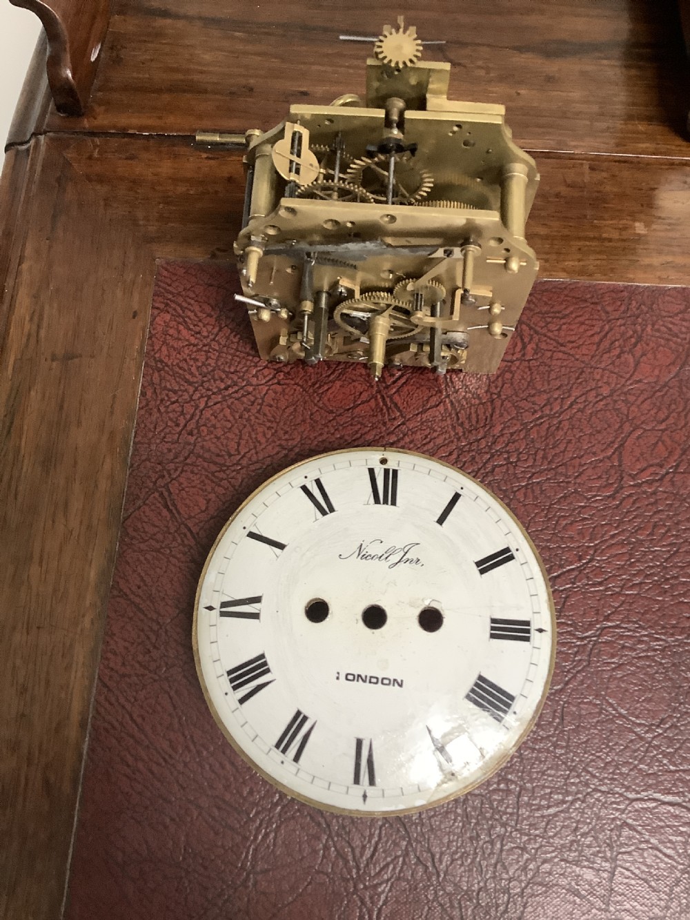 A Regency period wooden table clock with brass inlay, a pediment top, brass lion-head side handles, and a white dial displaying Roman numerals. View XII
