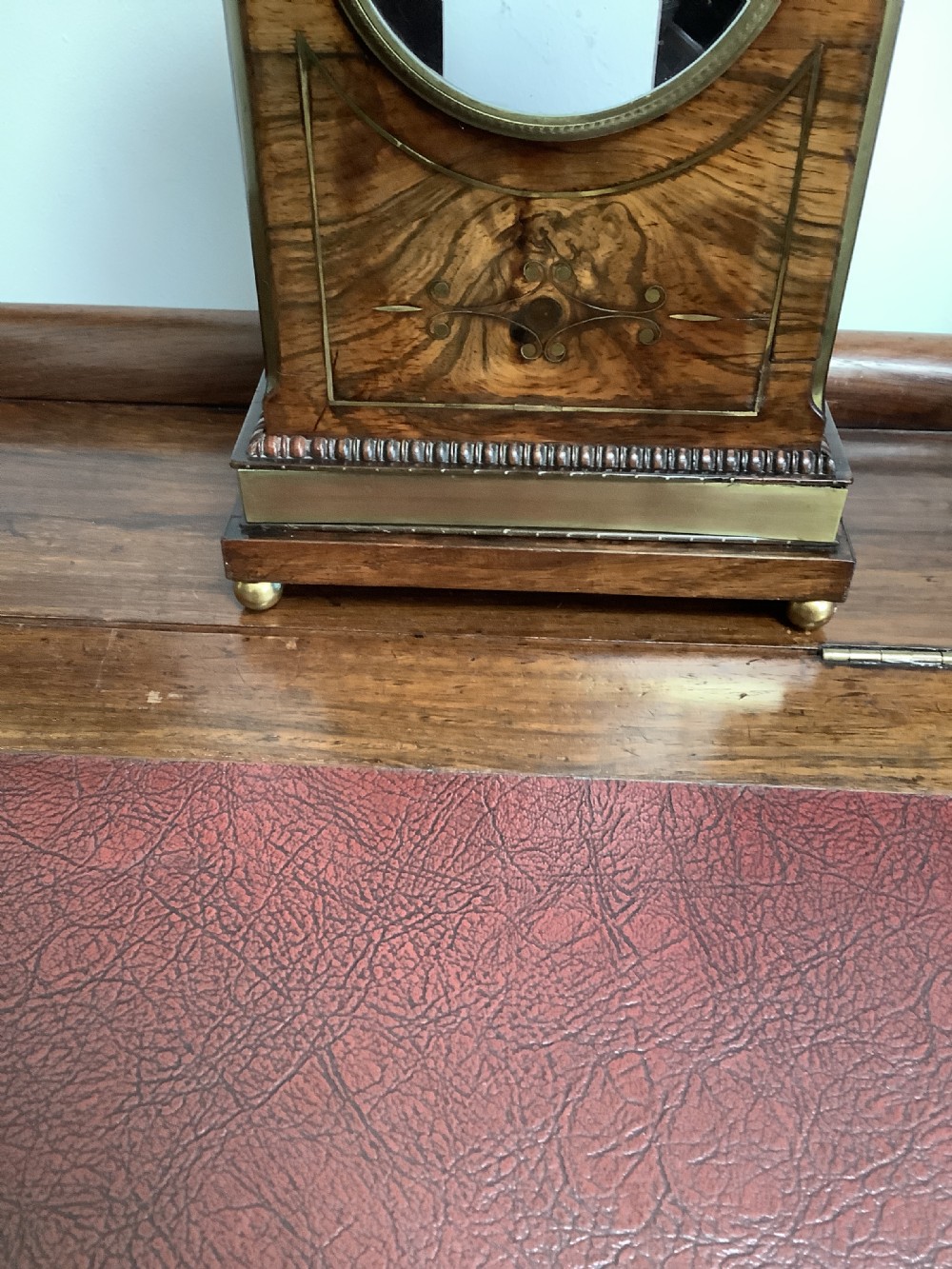 A Regency period wooden table clock with brass inlay, a pediment top, brass lion-head side handles, and a white dial displaying Roman numerals. View XVIII