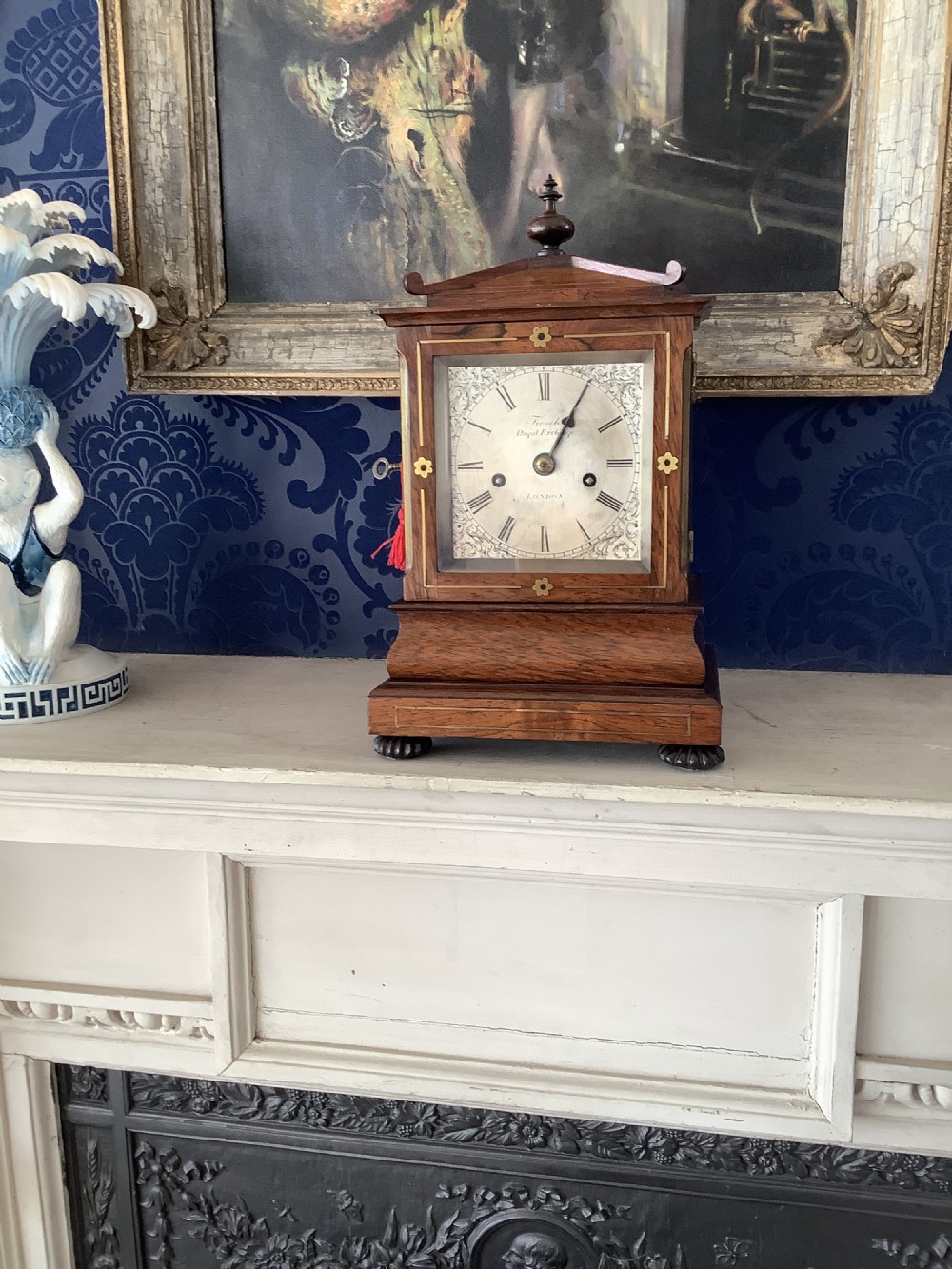 An antique rosewood table clock featuring brass inlay stringing, floral rosette mounts, a silvered square dial with Roman numerals, and a top finial.