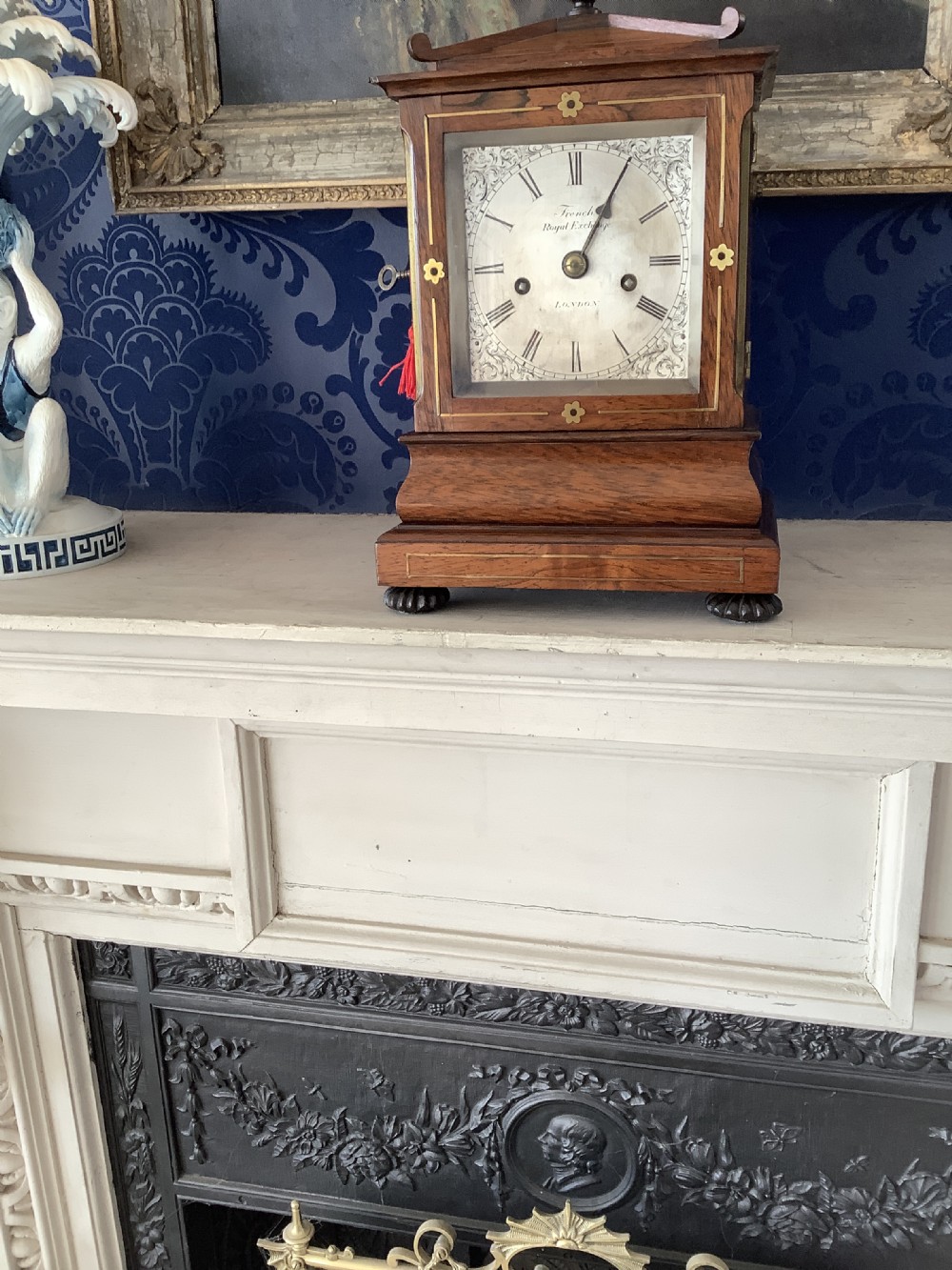 An antique rosewood table clock featuring brass inlay stringing, floral rosette mounts, a silvered square dial with Roman numerals, and a top finial. View II