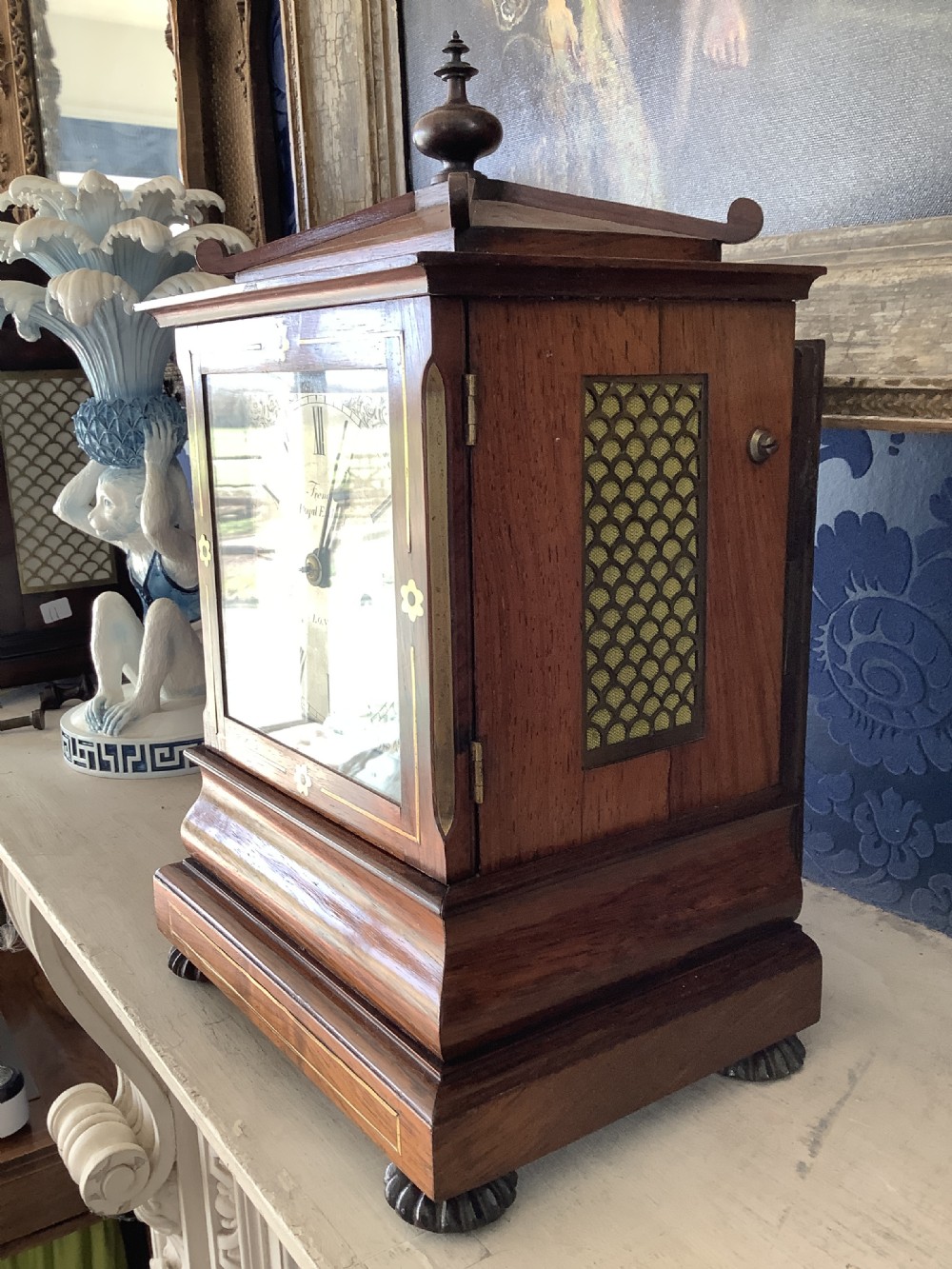 An antique rosewood table clock featuring brass inlay stringing, floral rosette mounts, a silvered square dial with Roman numerals, and a top finial. View III