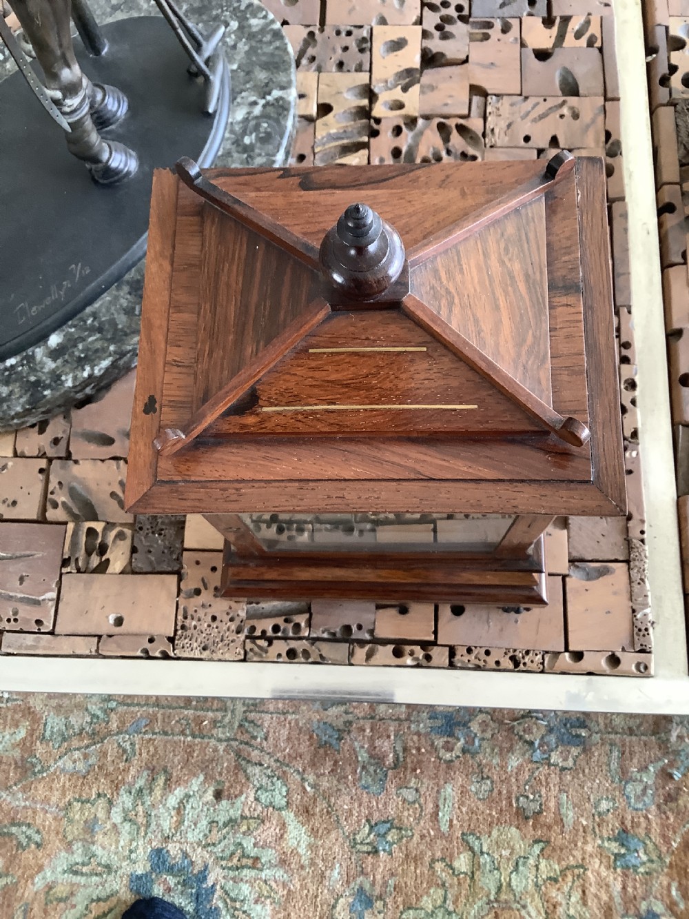 An antique rosewood table clock featuring brass inlay stringing, floral rosette mounts, a silvered square dial with Roman numerals, and a top finial. View IV