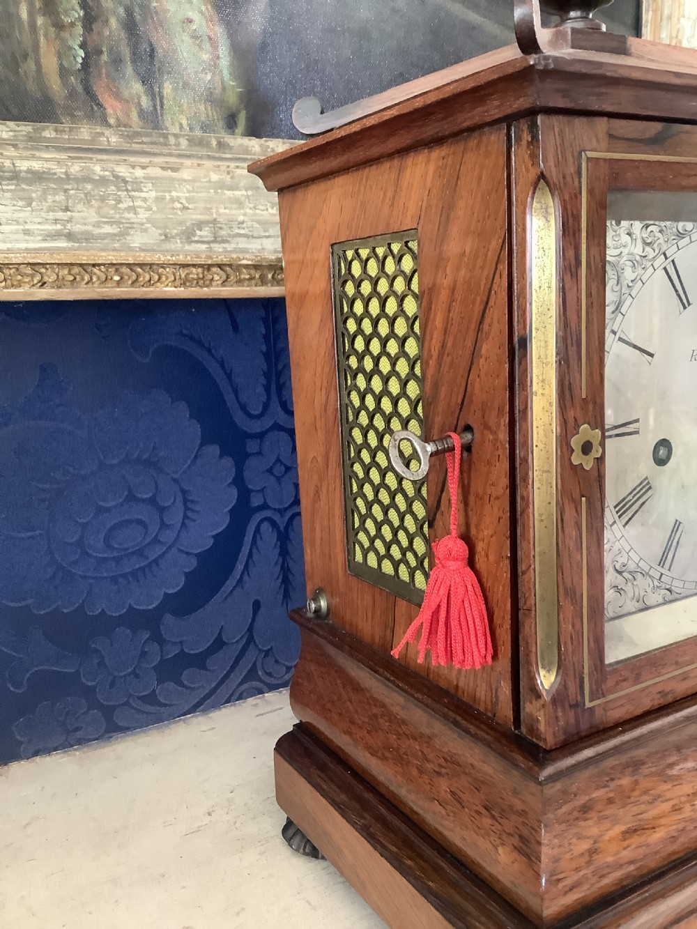 An antique rosewood table clock featuring brass inlay stringing, floral rosette mounts, a silvered square dial with Roman numerals, and a top finial. View VI