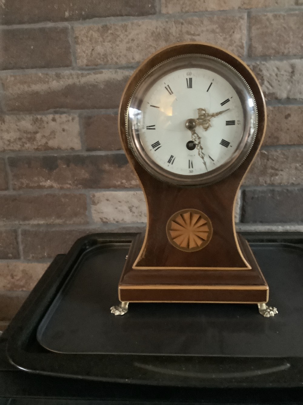 An antique French balloon-shaped wooden mantel clock featuring mahogany veneer with satinwood starburst marquetry inlay, a white dial with Roman numerals, and brass bracket feet. View II