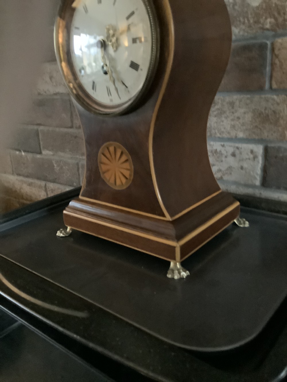 An antique French balloon-shaped wooden mantel clock featuring mahogany veneer with satinwood starburst marquetry inlay, a white dial with Roman numerals, and brass bracket feet. View VII