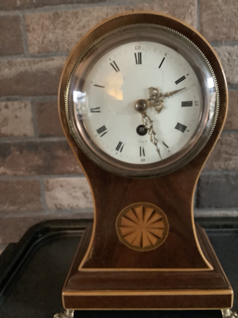 An antique French balloon-shaped wooden mantel clock featuring mahogany veneer with satinwood starburst marquetry inlay, a white dial with Roman numerals, and brass bracket feet. View VIII