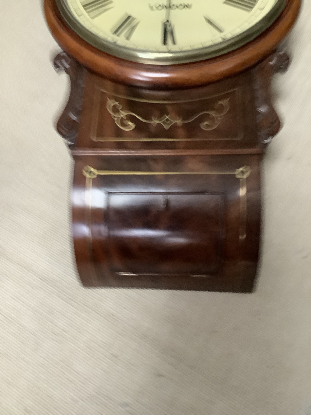 An antique Victorian mahogany drop dial wall clock featuring brass string inlay, carved side ears, and Roman numerals on a cream dial. View II