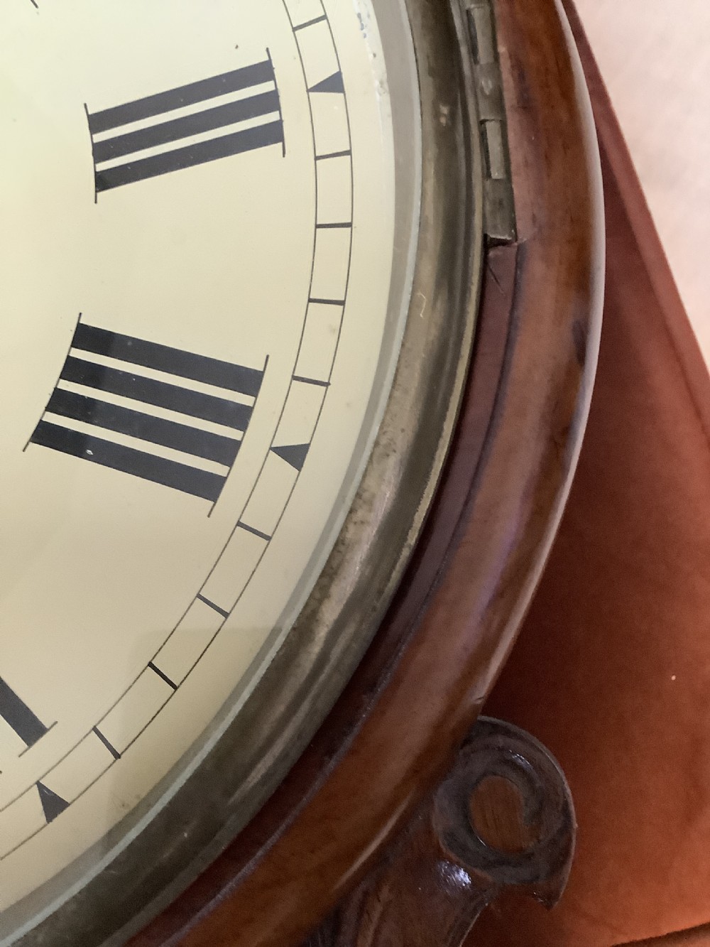 An antique Victorian mahogany drop dial wall clock featuring brass string inlay, carved side ears, and Roman numerals on a cream dial. View IV