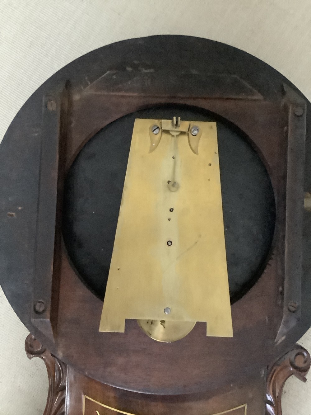 An antique Victorian mahogany drop dial wall clock featuring brass string inlay, carved side ears, and Roman numerals on a cream dial. View V