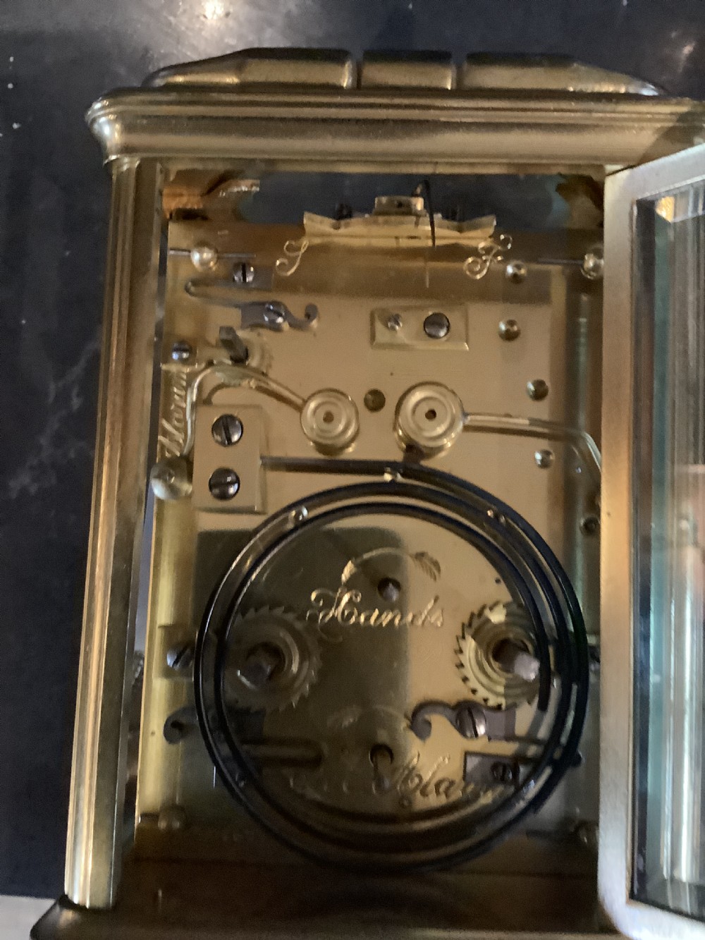 A square dark brown leather travelling case with a front window displaying a white clock dial with black Roman numerals and a small subsidiary dial. View IV