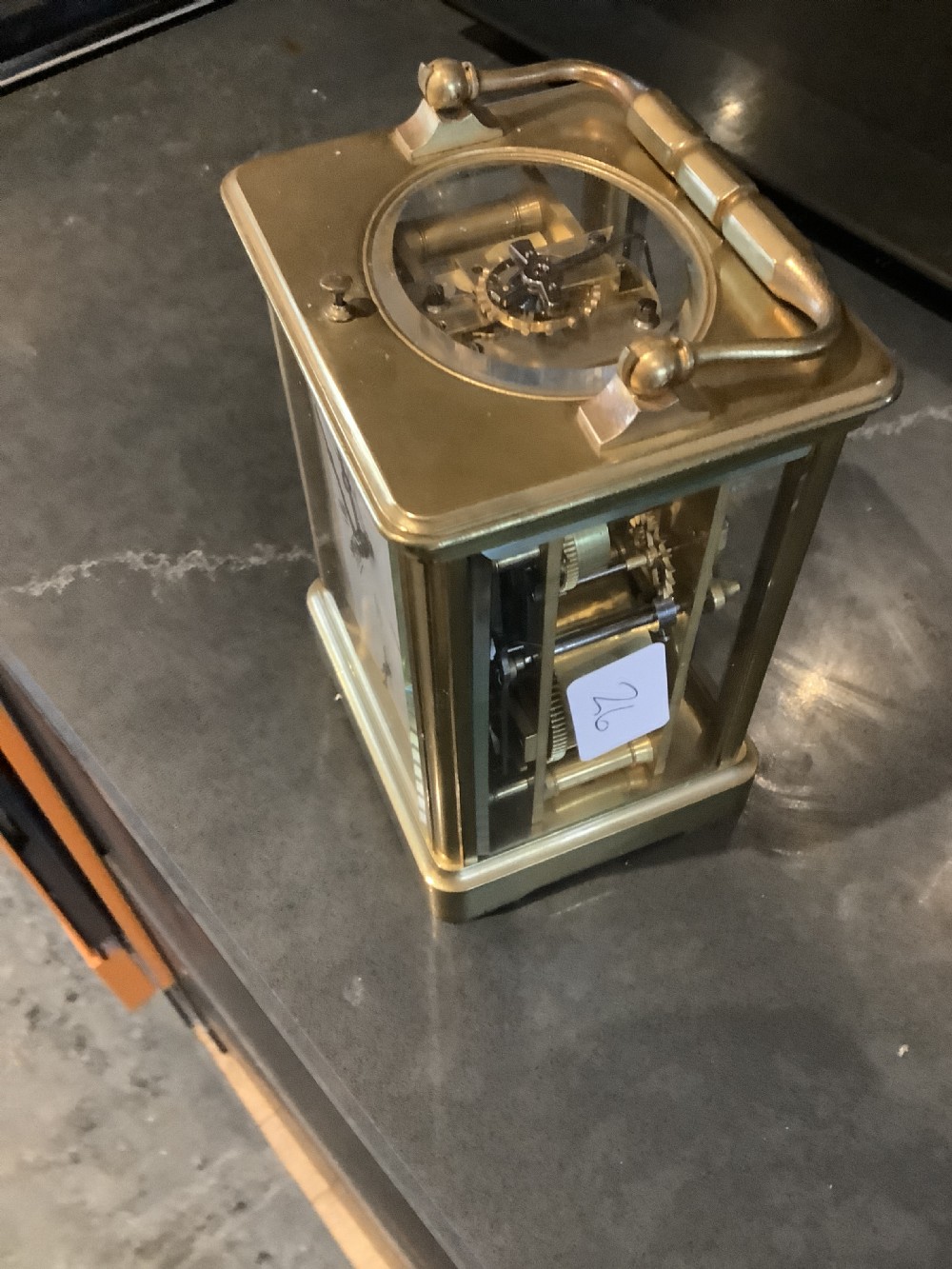 A square dark brown leather travelling case with a front window displaying a white clock dial with black Roman numerals and a small subsidiary dial. View VII