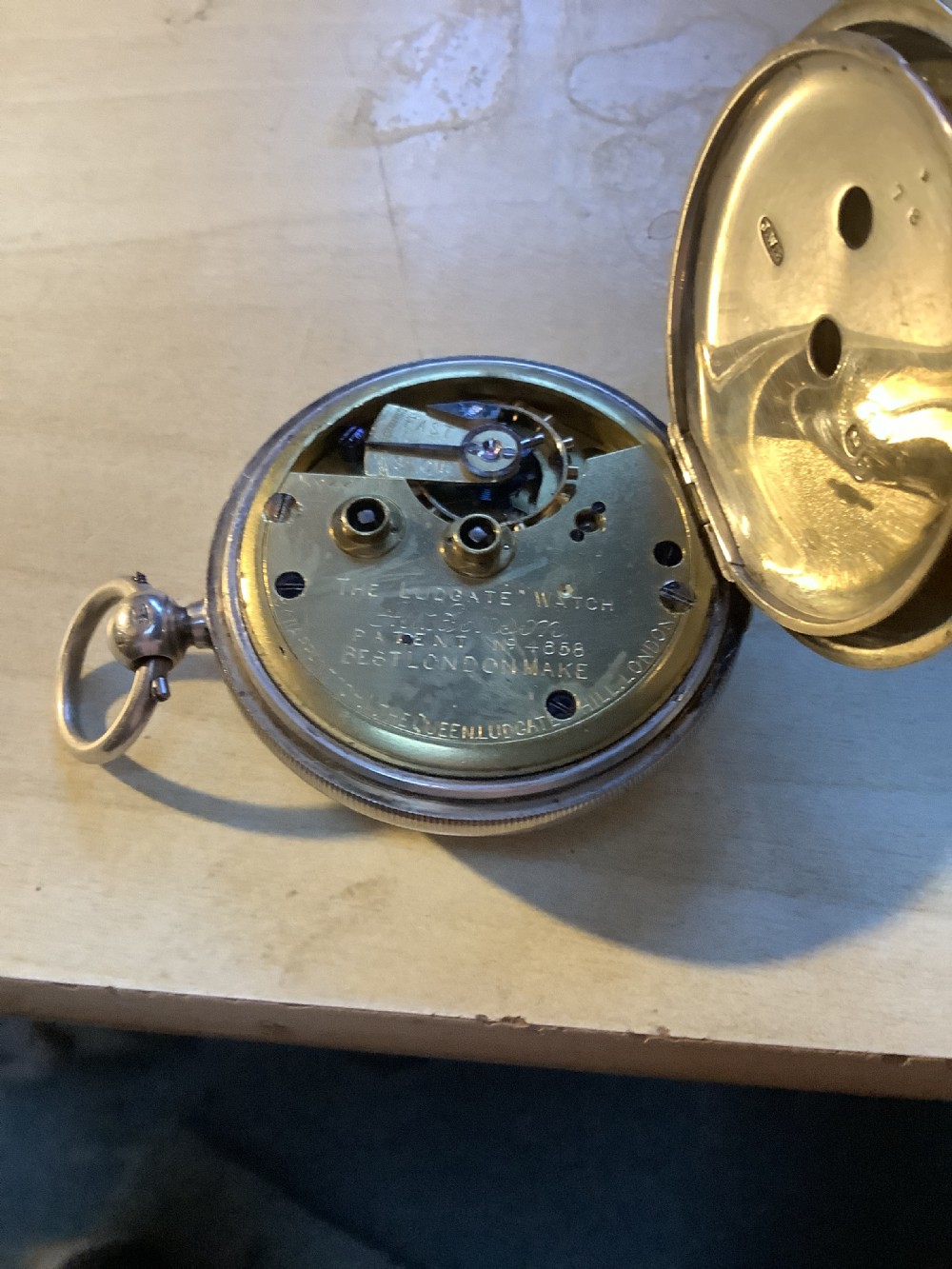 An antique pocket watch with a white enamel dial and Roman numerals displayed open inside a velvet-lined wooden presentation box. View II