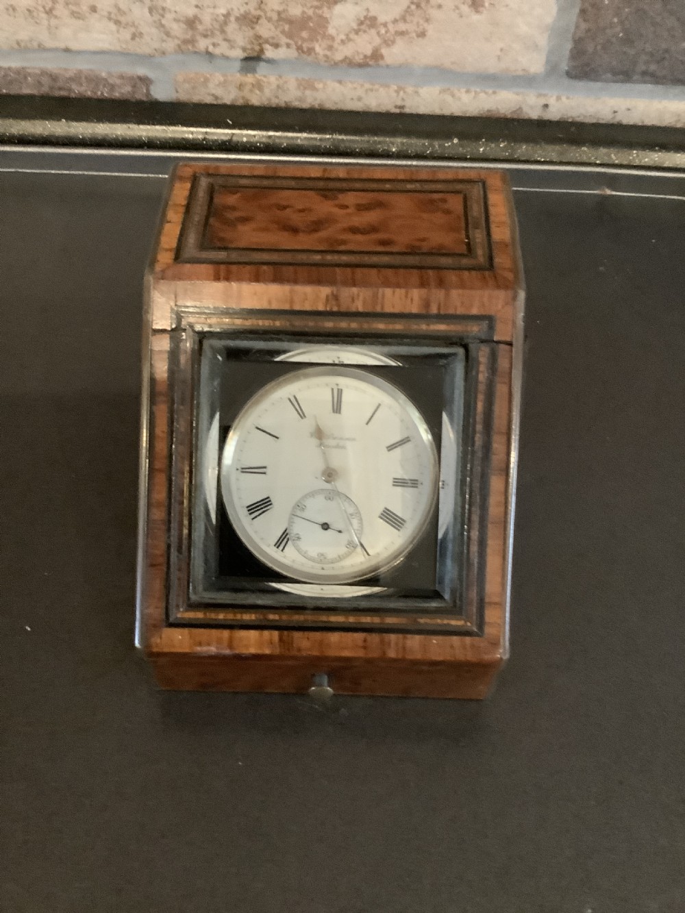 An antique pocket watch with a white enamel dial and Roman numerals displayed open inside a velvet-lined wooden presentation box. View VII