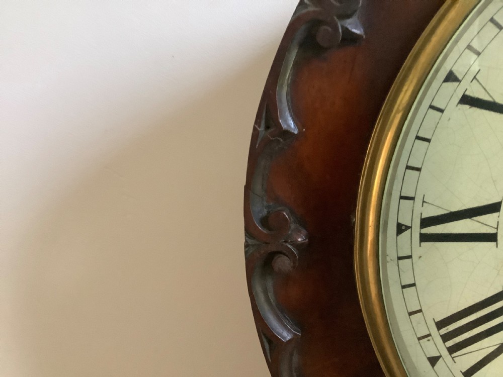 A Victorian carved mahogany fusee wall clock featuring an off-white circular dial with Roman numerals, brass bezel, and ornate matching wooden bracket support. View II