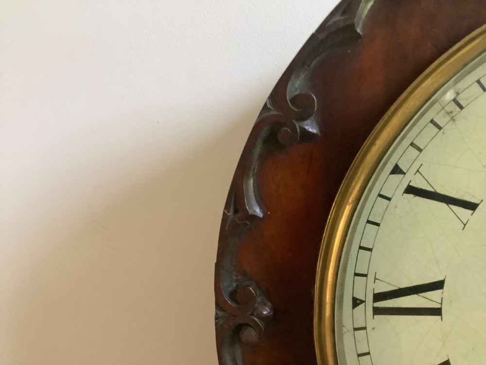 A Victorian carved mahogany fusee wall clock featuring an off-white circular dial with Roman numerals, brass bezel, and ornate matching wooden bracket support. View VIII