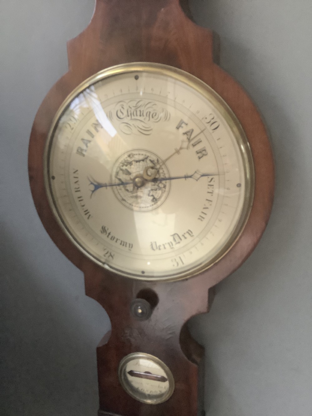 An antique wall-mounted mahogany banjo barometer featuring a swan-neck pediment, a central mercury thermometer tube, and a large circular silvered dial with brass rim. View III