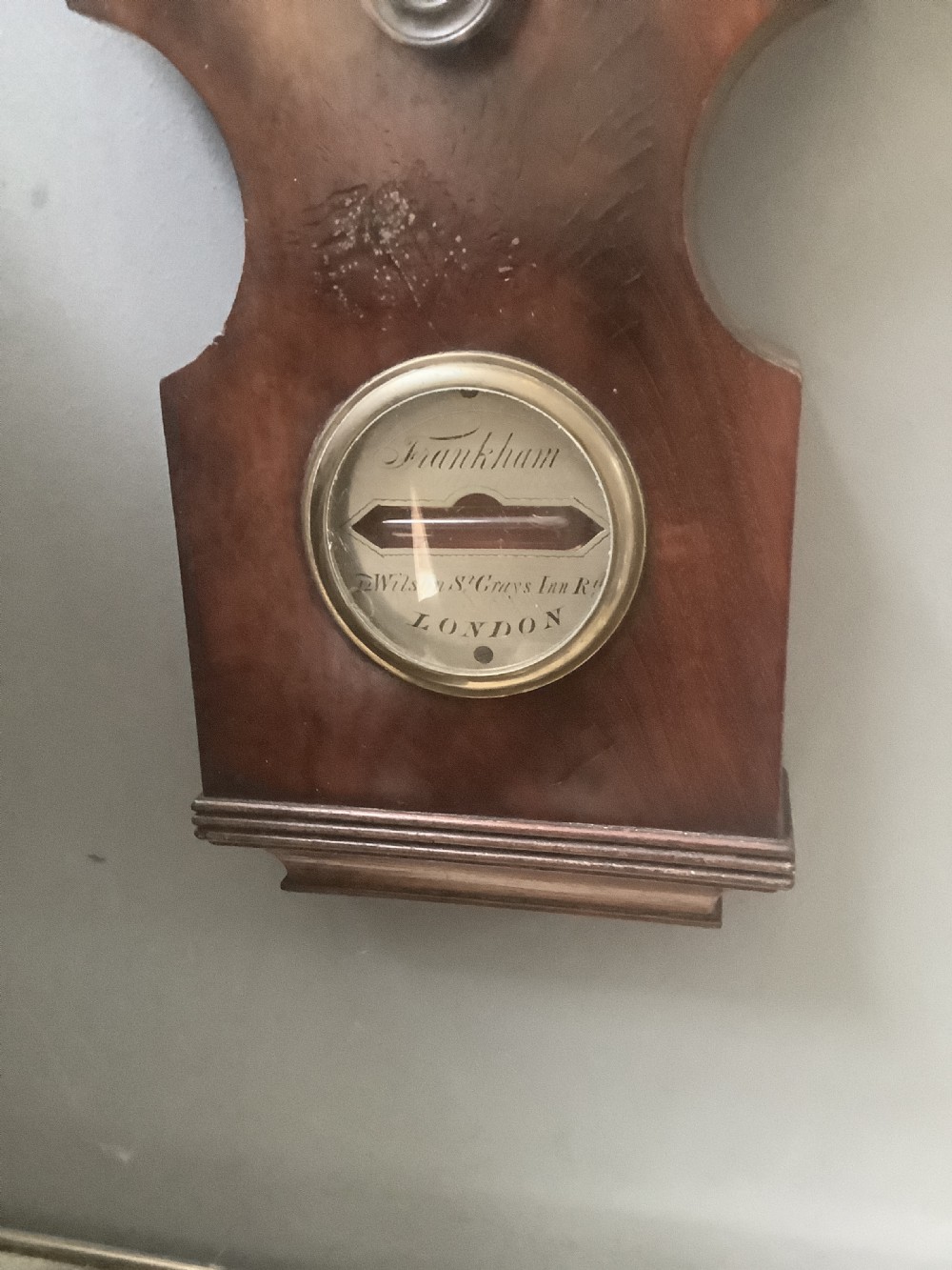 An antique wall-mounted mahogany banjo barometer featuring a swan-neck pediment, a central mercury thermometer tube, and a large circular silvered dial with brass rim. View V