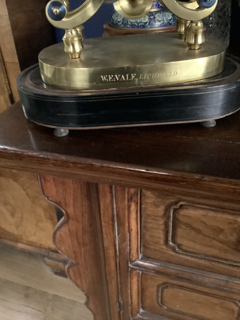 A Victorian brass skeleton clock featuring an openwork movement, a silvered chapter ring with Arabic numerals, and a engraved brass plinth resting on an ebonised oval base. View II