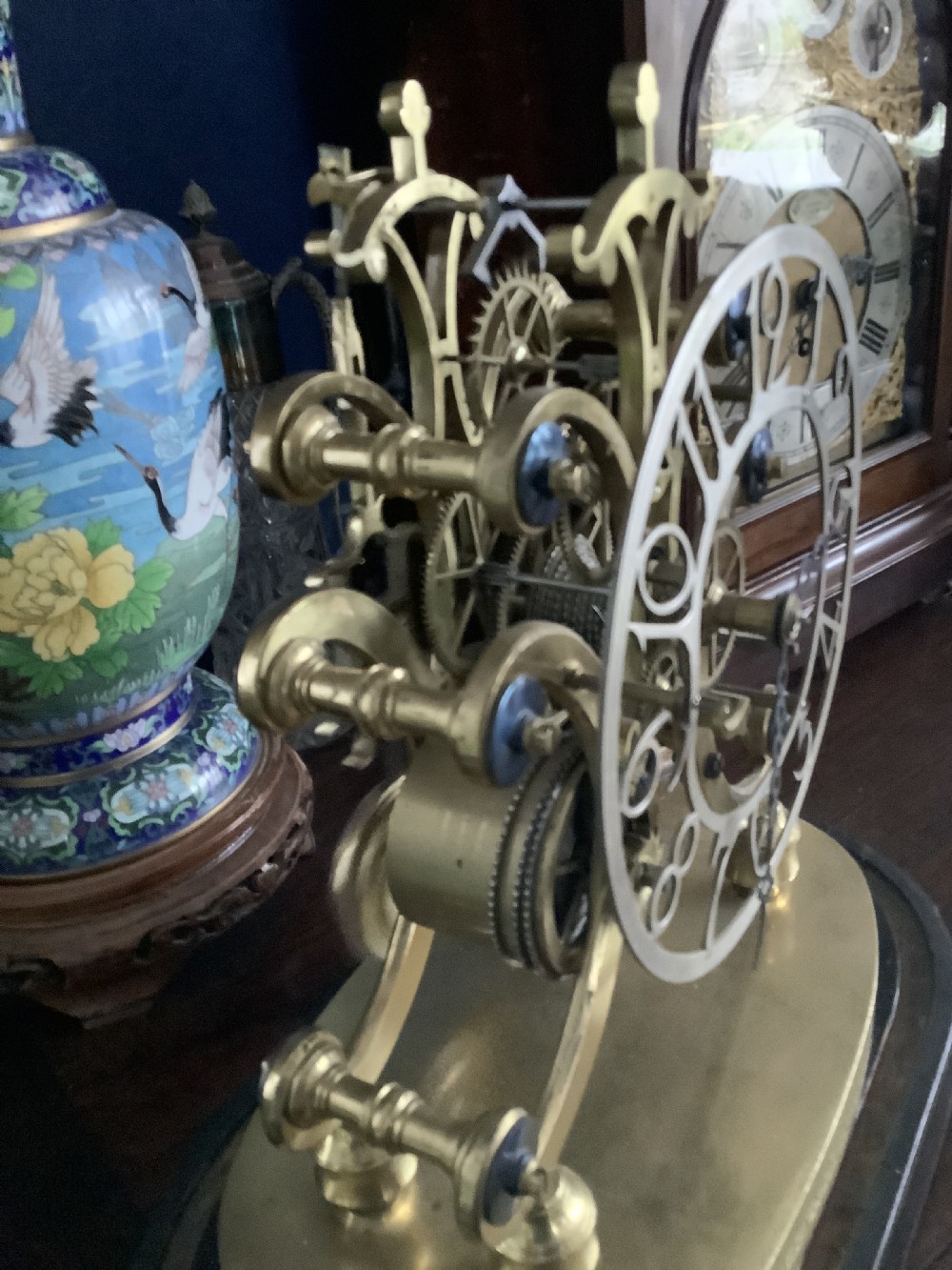 A Victorian brass skeleton clock featuring an openwork movement, a silvered chapter ring with Arabic numerals, and a engraved brass plinth resting on an ebonised oval base. View III