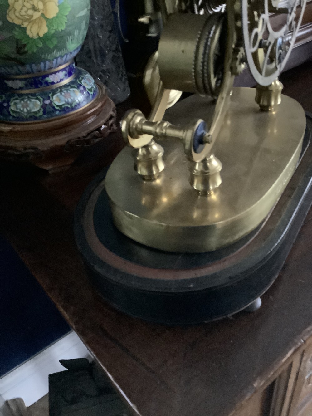 A Victorian brass skeleton clock featuring an openwork movement, a silvered chapter ring with Arabic numerals, and a engraved brass plinth resting on an ebonised oval base. View IV