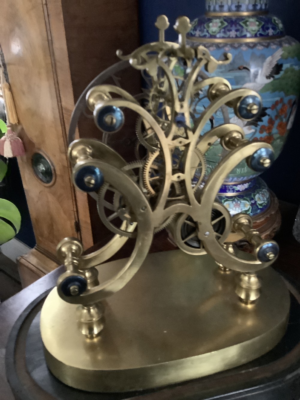 A Victorian brass skeleton clock featuring an openwork movement, a silvered chapter ring with Arabic numerals, and a engraved brass plinth resting on an ebonised oval base. View V