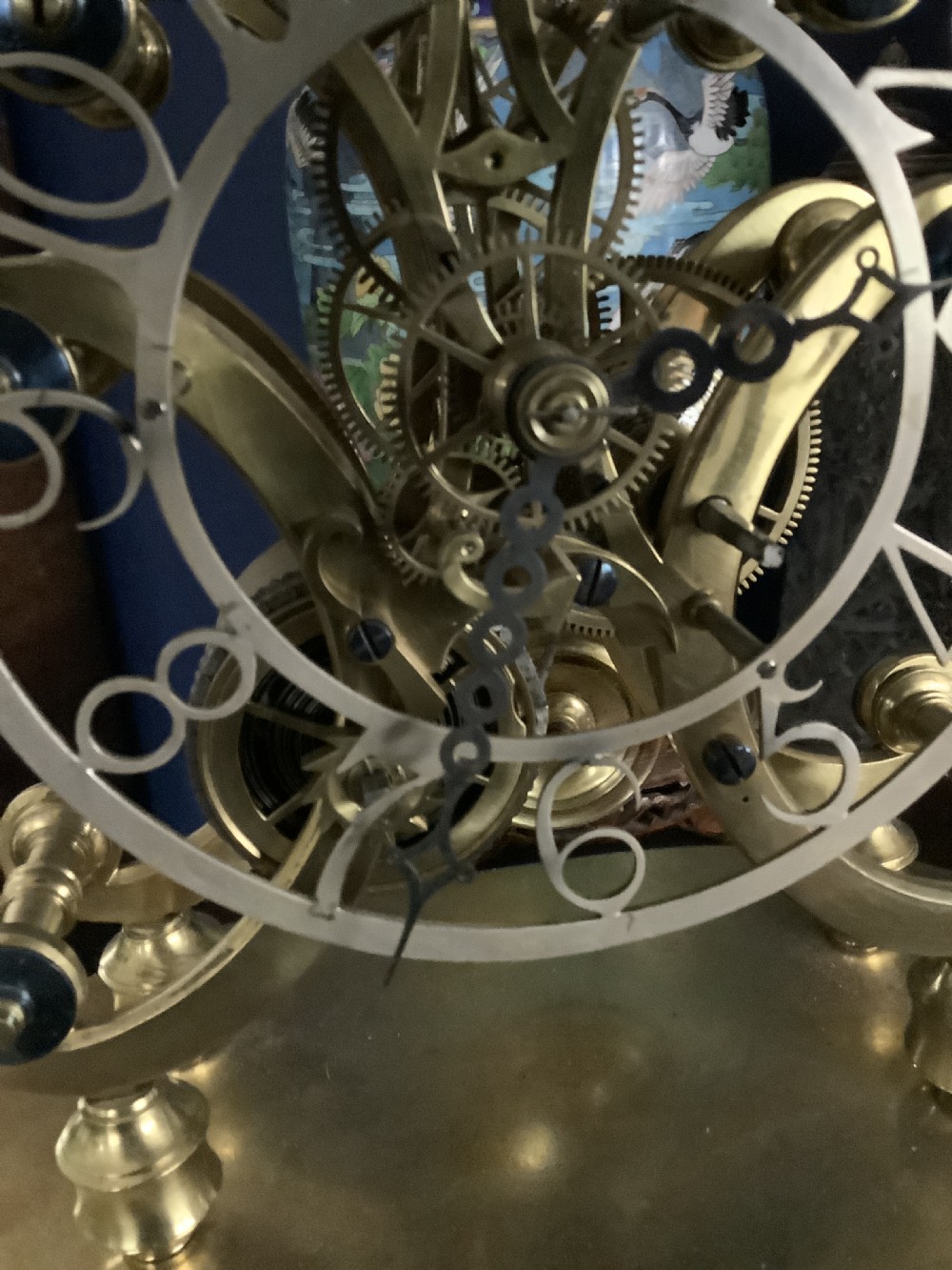 A Victorian brass skeleton clock featuring an openwork movement, a silvered chapter ring with Arabic numerals, and a engraved brass plinth resting on an ebonised oval base. View VI