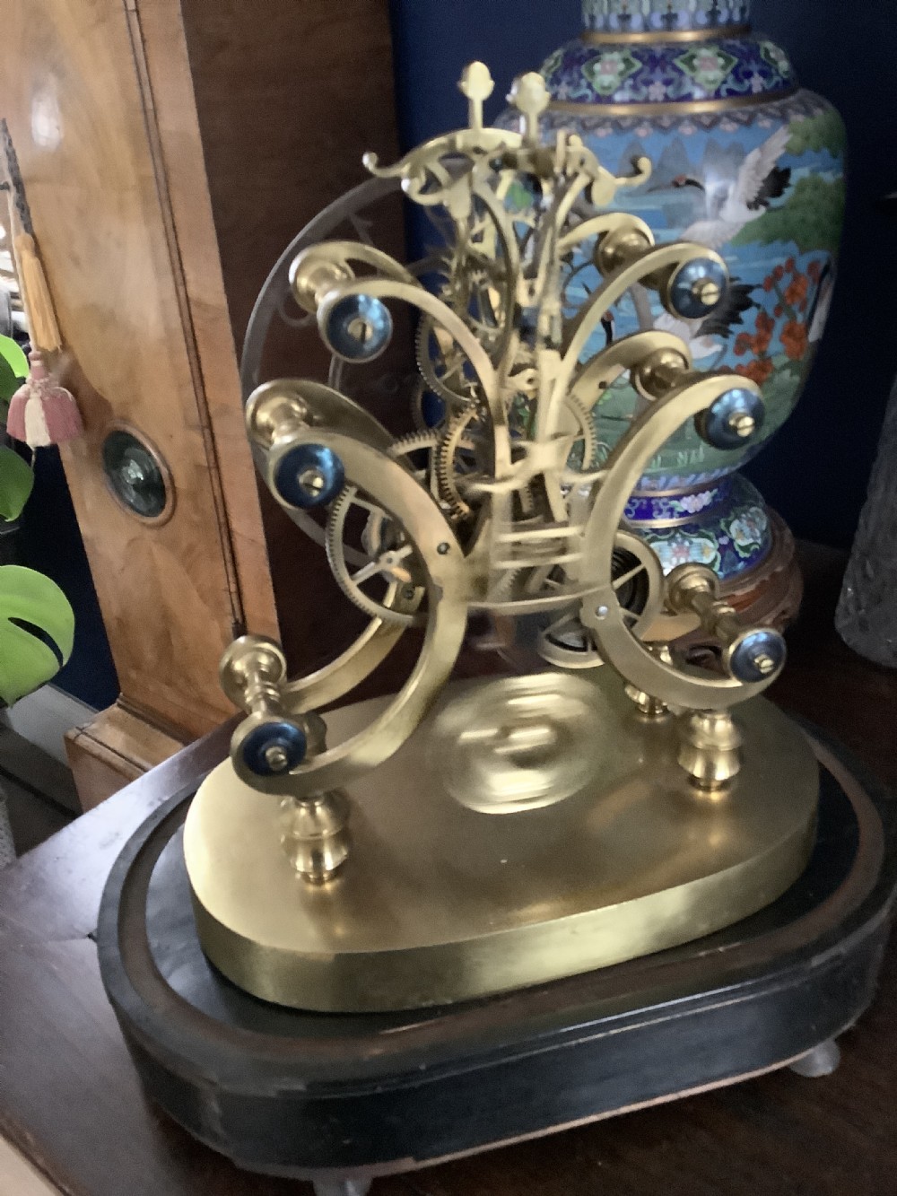 A Victorian brass skeleton clock featuring an openwork movement, a silvered chapter ring with Arabic numerals, and a engraved brass plinth resting on an ebonised oval base. View VIII