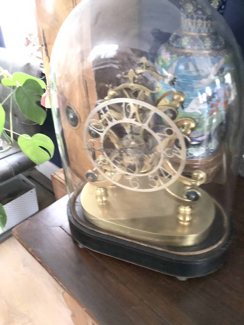 A Victorian brass skeleton clock featuring an openwork movement, a silvered chapter ring with Arabic numerals, and a engraved brass plinth resting on an ebonised oval base. View X