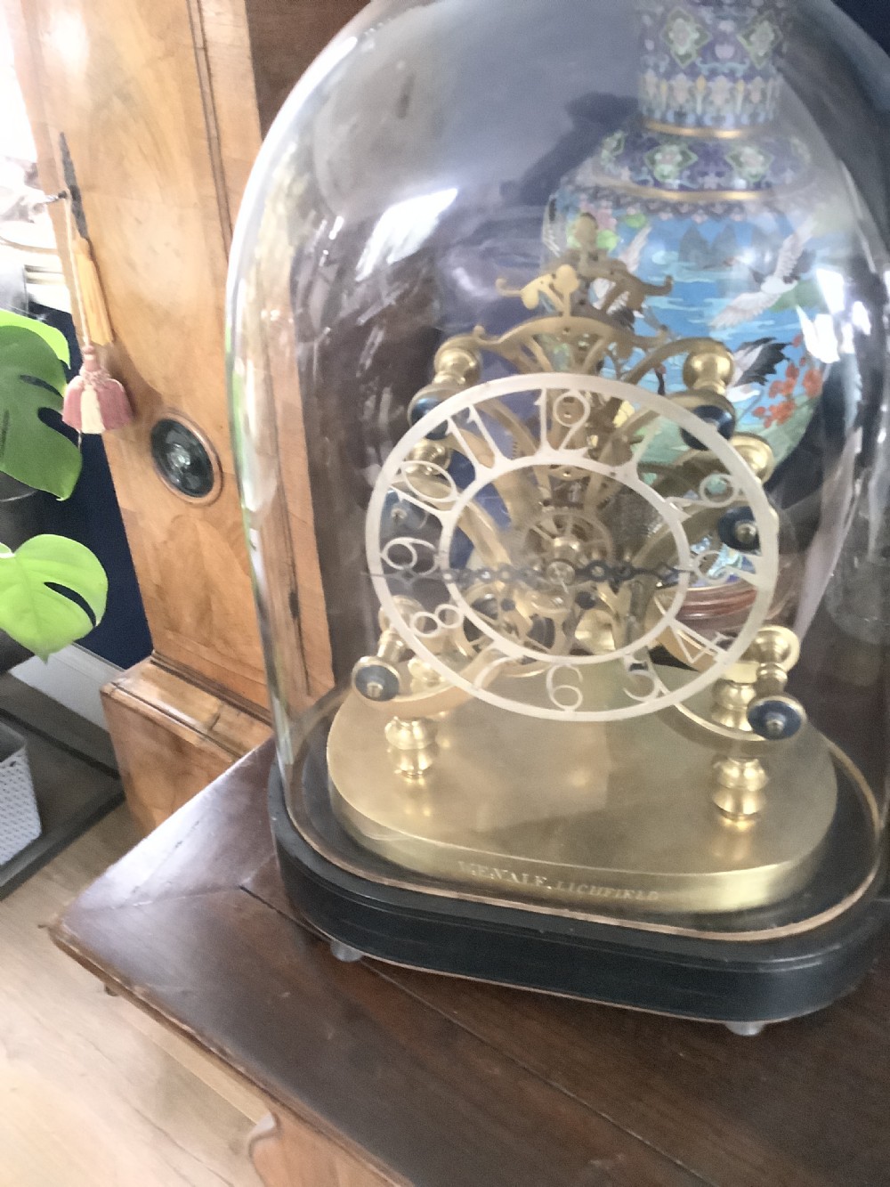 A Victorian brass skeleton clock featuring an openwork movement, a silvered chapter ring with Arabic numerals, and a engraved brass plinth resting on an ebonised oval base. View XI