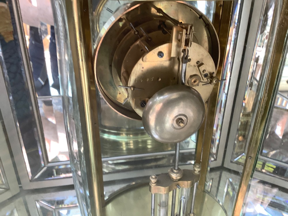 An oval brass four glass mantel clock featuring an enamel dial with Roman numerals and visible internal escapement mechanism. View IV