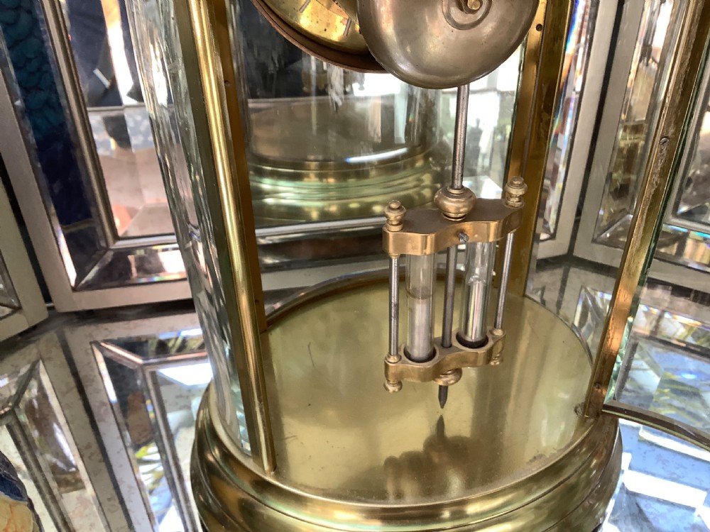 An oval brass four glass mantel clock featuring an enamel dial with Roman numerals and visible internal escapement mechanism. View V