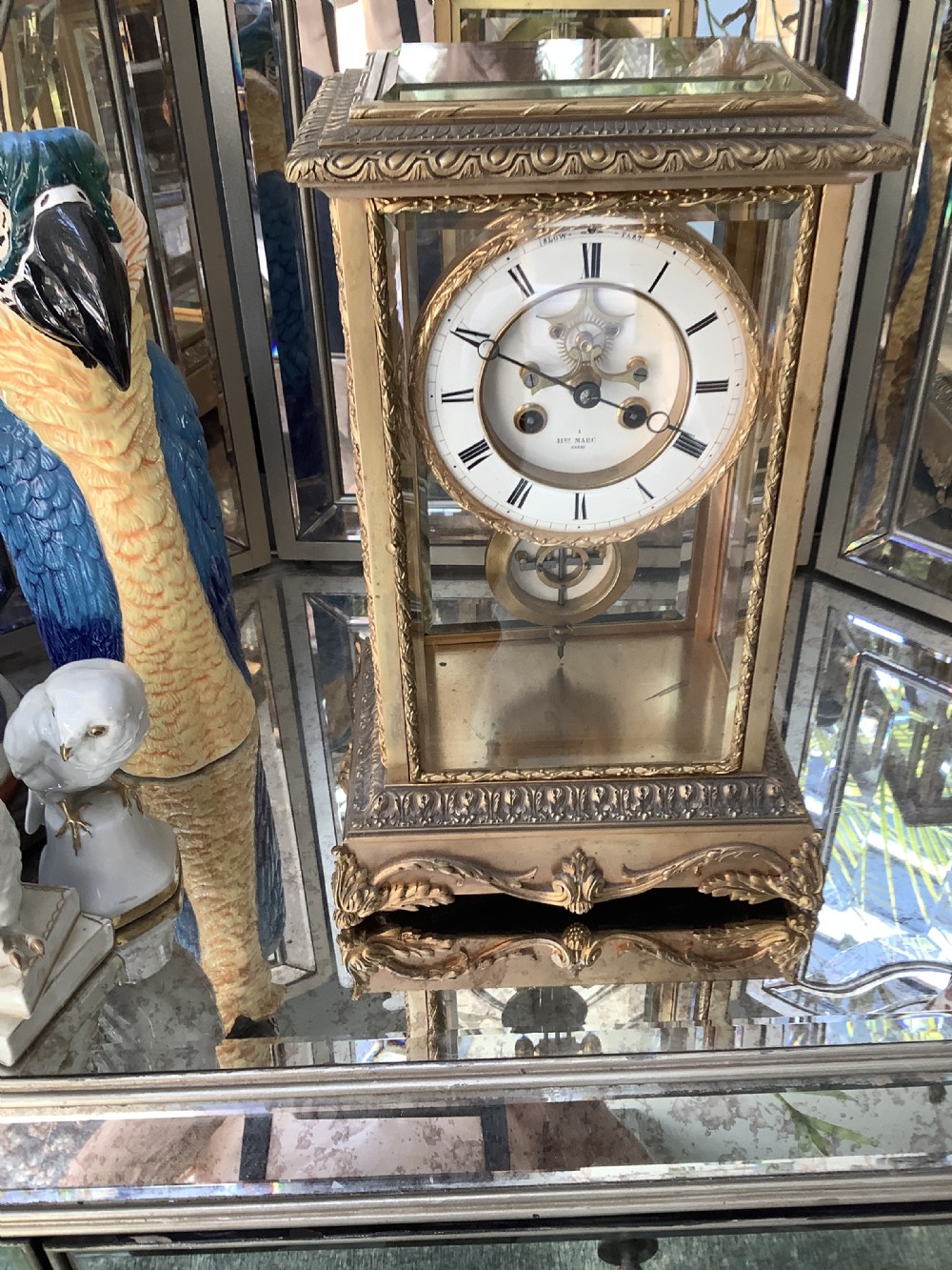 A 19th-century French four-glass mantel clock featuring a gilt brass case with decorative moulding, bevelled glass panels, a white enamel dial with Roman numerals, and a visible mercury pendulum.