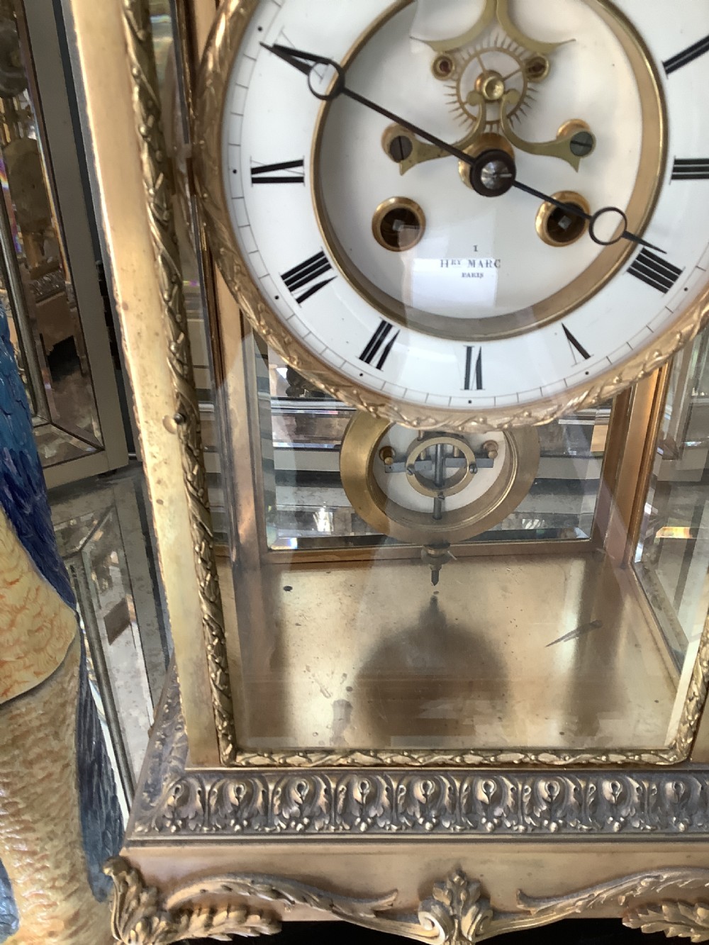 A 19th-century French four-glass mantel clock featuring a gilt brass case with decorative moulding, bevelled glass panels, a white enamel dial with Roman numerals, and a visible mercury pendulum. View II