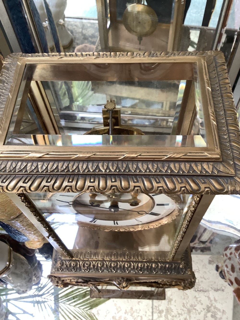 A 19th-century French four-glass mantel clock featuring a gilt brass case with decorative moulding, bevelled glass panels, a white enamel dial with Roman numerals, and a visible mercury pendulum. View IV
