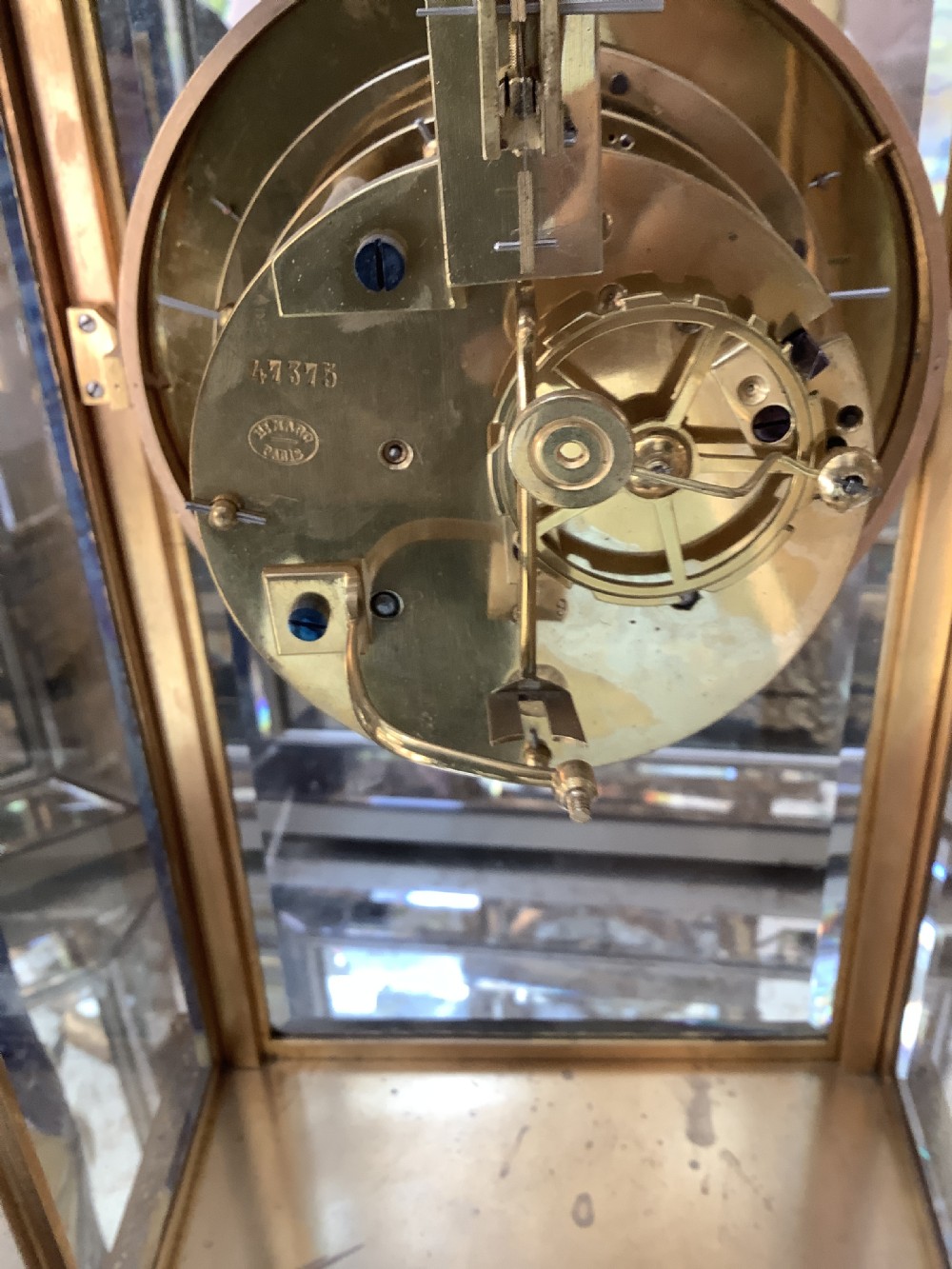 A 19th-century French four-glass mantel clock featuring a gilt brass case with decorative moulding, bevelled glass panels, a white enamel dial with Roman numerals, and a visible mercury pendulum. View V